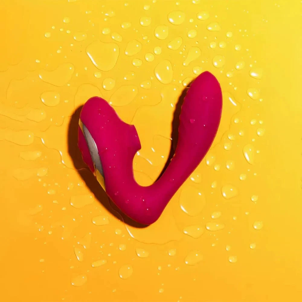 Pink clitoral suction stimulator with dual-function vibrator on wet yellow surface.